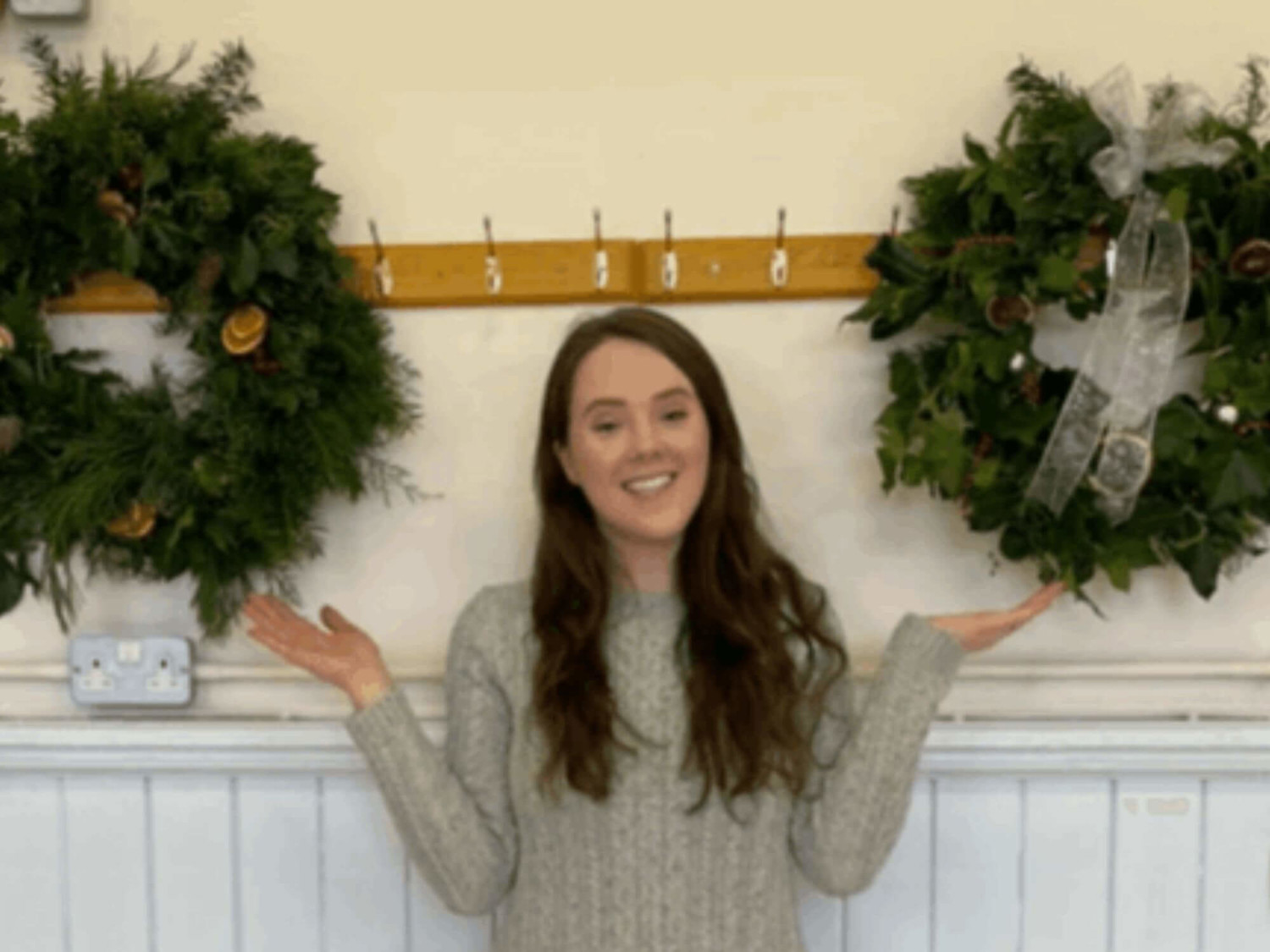 Girl holding hands up to Christmas wreathes on wall
