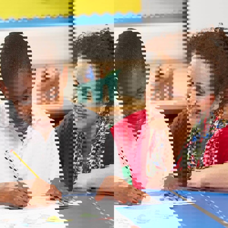 Boy writing with teacher smiling next to him